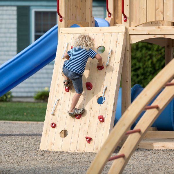 Boy climbing on climbing wall of commercial outdoor playset